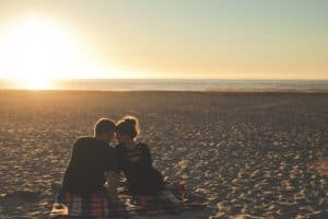 Couple sitting on the sand at the beach - Cheap Date Ideas