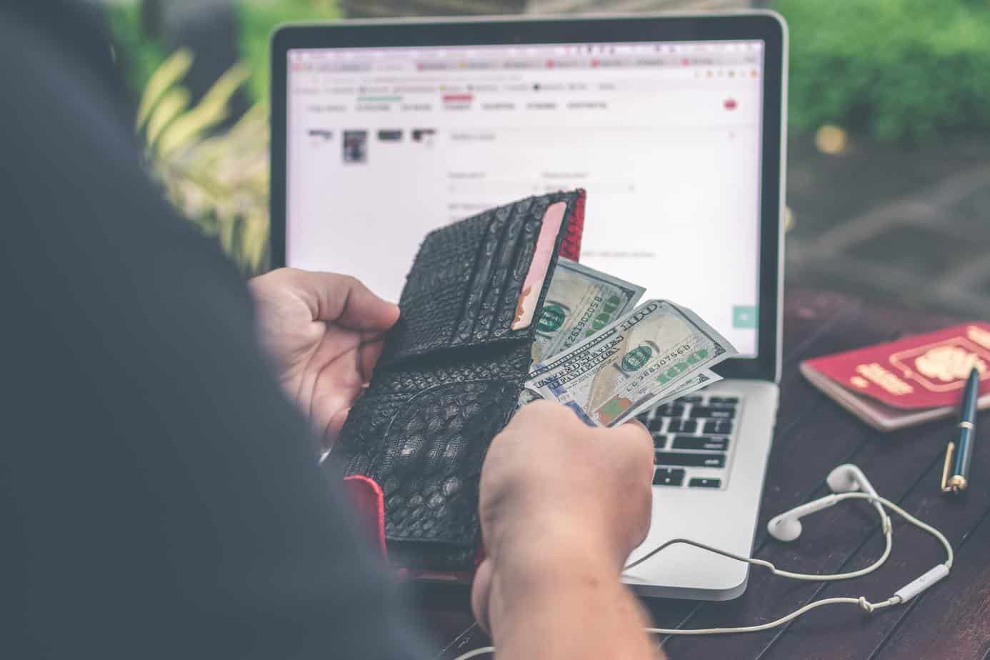 saving money - money in wallet and laptop on desk