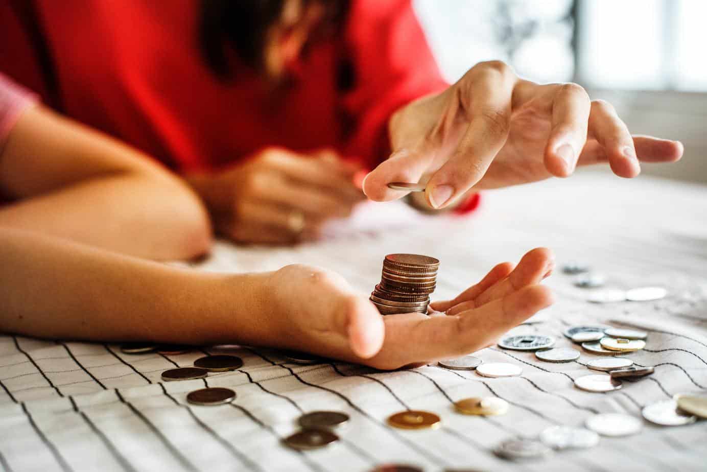 Two persons stacking and counting coins on a table - money saving challenge