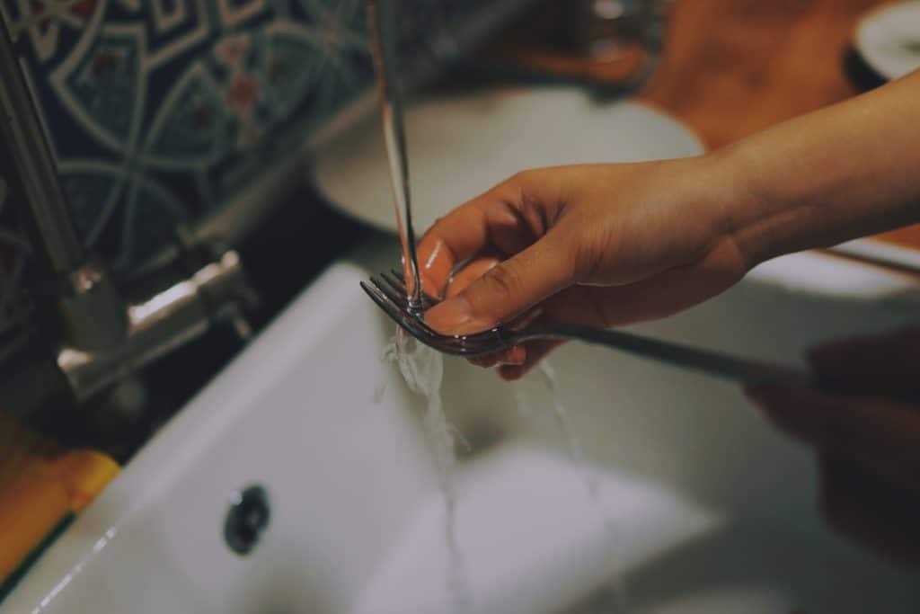 handwashing a fork over a kitchen sink - money saving tips for the kitchen