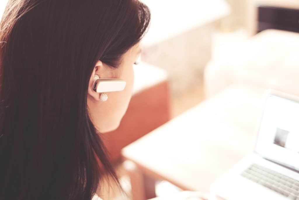 woman working on laptop with headphones in ear - best transcription companies that hire beginners