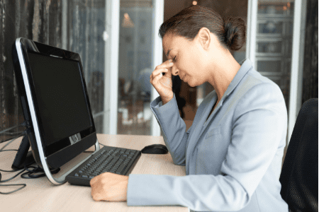 woman with headache at desk - occupational burnout