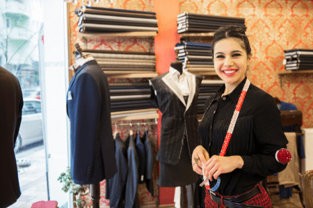 dress alterations near me - female tailor smiling with rolls of cloth in background