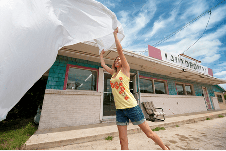 coin laundry near me - young woman with bed sheet in front of laundromat