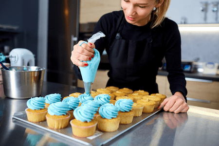 woman frosting cupcakes and thinking of pricing of cupcakes