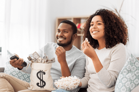 man and woman watching tv with popcorn and money