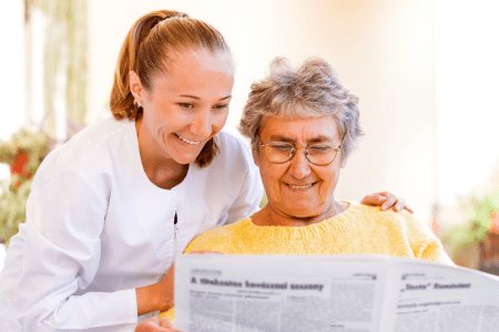elderly woman reading newspaper with younger woman behind
