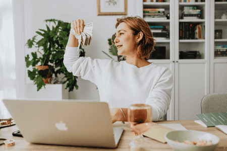 woman holding cash using laptop for quick pay survey sites
