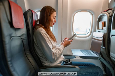 young lady sitting at window seat in airplane with phone in hand